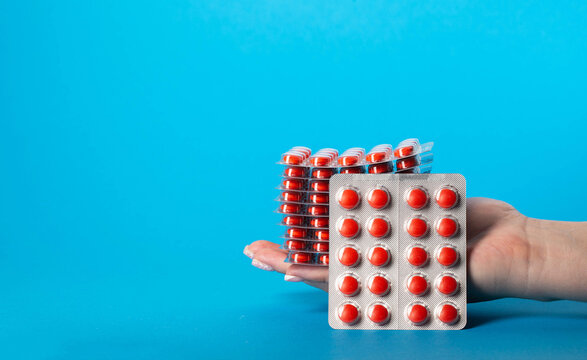 Stack of red pills in hand on blue background for edema. Diuretic pills for urethritis. Copy space for text, metabolism