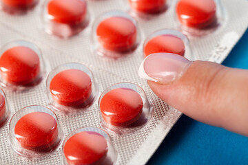 Woman's finger with manicure on a blister with red pills. Concept of nootropic pills, sedative pills, macro
