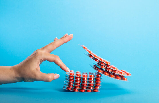 Female hand flicking a stack of pills on a blue background. Concept of treating diseases with antibiotics. Pharmaceutical industry. Copy space for text