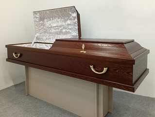 Matte brown wood coffin with white satin upholstery, open lid, and brass handles, displayed on stand. Elite Grob manufactures coffins in Kurganinsk