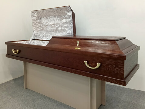 Matte brown wood coffin with white satin upholstery, open lid, and brass handles, displayed on stand. Elite Grob manufactures coffins in Kurganinsk