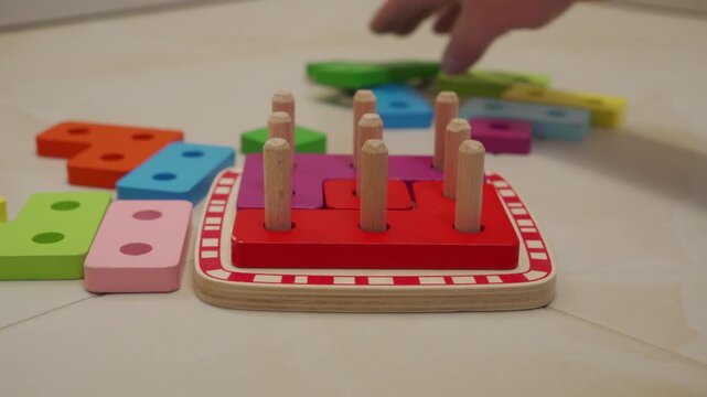 A hand slides a wooden shape-sorting puzzle into place on a hard tile floor. The wood drags across the floor, producing a short, low scrape.