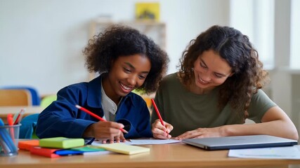 Two smiling diverse women sitting together at a classroom desk, with a teacher assisting a young student with her notes during a tutoring session, promoting education and mentorship - Powered by Adobe