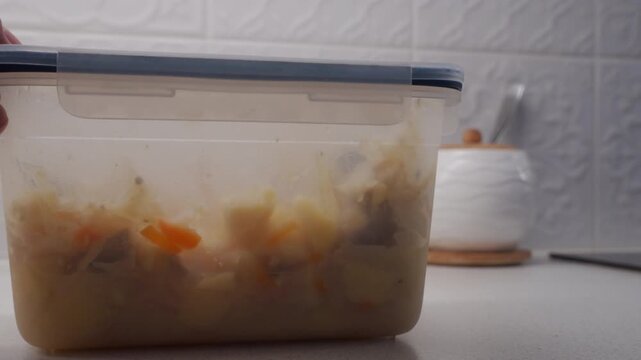 A plastic food container with stew inside is pushed along a smooth kitchen counter. The plastic base drags on the surface, producing a soft scrape.