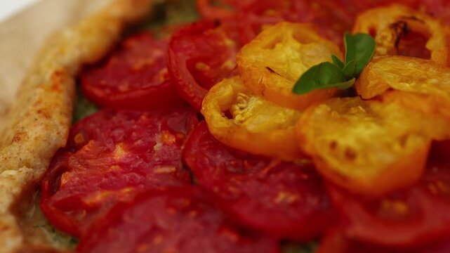 A delicious tomato galette is displayed on parchment paper, showcasing layers of vibrant red and yellow tomatoes atop a flaky crust in a warm kitchen atmosphere.