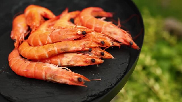 Freshly grilled shrimp rest on a black grill plate, with vibrant green grass providing a lively backdrop in a sunny outdoor environment, suggesting a barbecue gathering.