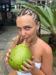 Young woman holding a fresh green coconut in front of lush tropical greenery. Vibrant summer atmosphere, travel lifestyle, exotic vacation mood, nature background.