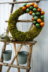 Moss wreath with Christmas baubles standing on rustic ladder