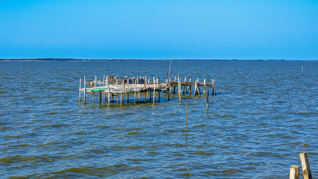 Traditional wooden fishing pier, an old stilt house used for fishing on Lesina Lake in Gargano, Puglia, Italy. Calm water and clear blue sky on a sunny day. Travel and tourism concept.