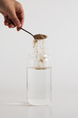 Psyllium pouring from a silver spoon into a glass of water on a white background