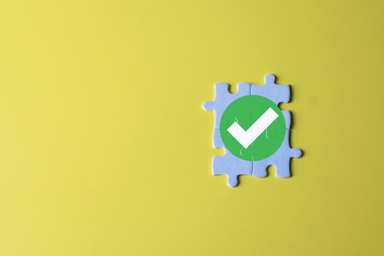 Solution, quality assurance, and completion concept. Assembled puzzle pieces with a green checkmark icon, symbolizing approval, success, and a problem solved on a yellow background with copy space. - Powered by Adobe