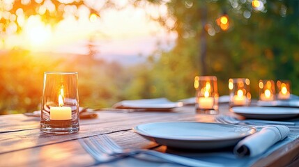 An outdoor dining table is set with plates, cutlery, and lit candles in glass holders, bathed in the warm glow of a sunset.