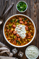 Potato soup with sausage and yogurt on wooden table. Top view