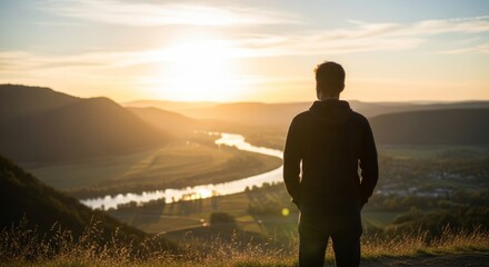 Young caucasian male watching serene river valley sunset amidst rolling hills