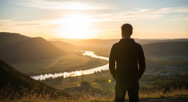 Young caucasian male watching serene river valley sunset amidst rolling hills