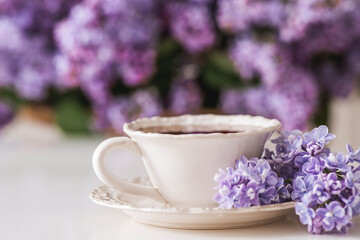 The concept of home comfort and drinks. A cup of tea or coffee on the table. In the background is a large purple bouquet of lilacs.