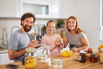 A family sits together in a well-lit kitchen, sharing breakfast and laughter. They enjoy various foods while the cheerful atmosphere enhances their bonding moment.