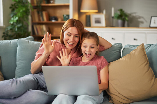 A joyful interaction takes place as a mother and daughter engage in a video call from their living room, smiling and waving to someone on the screen. Their excitement is evident.