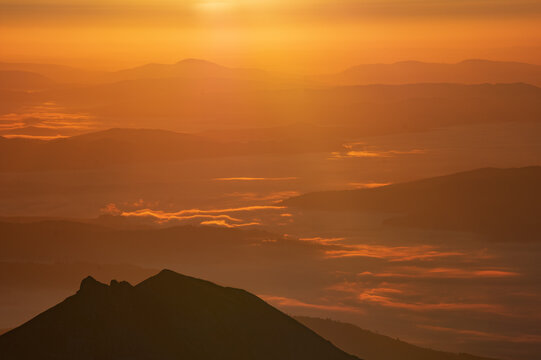 Aerial view of the Jahnaci stit peak, a silhouette against the glowing horizon, blanketed by ethereal mist, Vysoke Tatry, Presov Region, Slovakia.