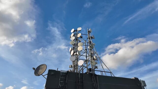 Rooftop base station with antennas, transmitter equipment and a satellite dish captured in a fast-moving cloud timelapse. Ideal for telecom, wireless network and infrastructure projects.