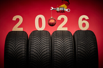 Winter car tires, big wheels service and hand of mechanic man with wrench and christmas ball on red background.