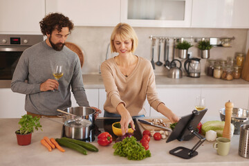 A couple enjoys preparing a meal in a bright kitchen, surrounded by fresh vegetables and utensils, while engaged in a joyful cooking experience.
