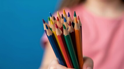 A child's hand holding a bunch of colored pencils. Close-up on art supplies for drawing and creativity against a blue background. Back to school concept - Powered by Adobe