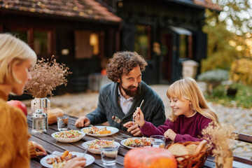 A family sits at a rustic table outside, sharing a delicious meal on a cool autumn weekend. Laughter and smiles fill the air as they savor each bite.