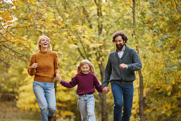 A family is having fun as they walk hand in hand through a park. The vibrant autumn foliage creates a cheerful backdrop for their joyful weekend outing.