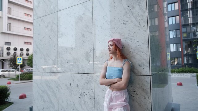 A portrait of a teenage girl with red hair posing for a photo near columns at the entrance to a business center