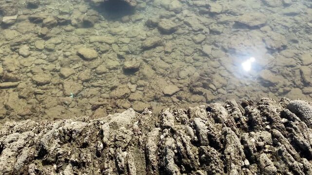 Sunlights sparkles on crystal clear tidal water beside the rough stone wall of the historic fish corrales in Chipiona on a calm Atlantic morning