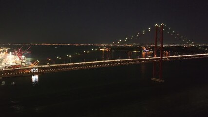 Aerial drone shot by iconic and famous 25th April Bridge, Ponte 25 de Abril, and Cristo Rei in Lisbon, Portugal, Europe. Night, waterfront, drone panning slowly