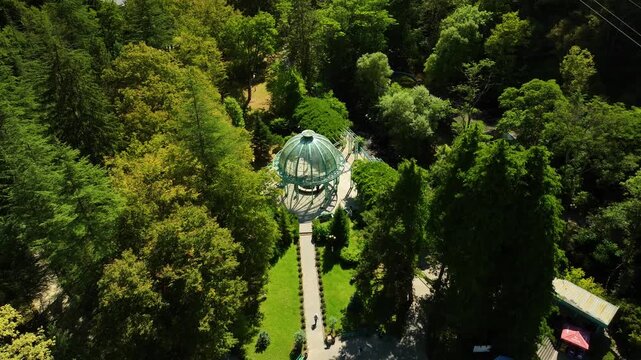 A direct aerial view of a circular glass pavilion surrounded by dense green forest, pathways, and well-organized garden landscaping.
