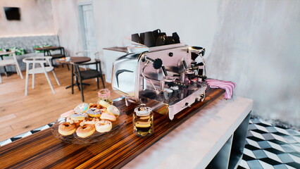 A charming cafe features a sleek coffee machine beside a platter of colorful pastries. Sunlight filters in, enhancing the warm, inviting atmosphere that encourages relaxation and enjoyment.