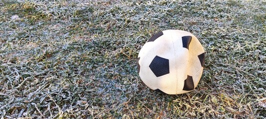 A deflated soccer ball lying on frosty green grass. Forgotten football on a cold winter morning field. End of the sports season concept