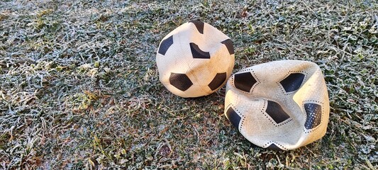 Two old deflated soccer balls on frosty grass in the cold winter morning. Abandoned footballs on a frozen field representing the end of a season