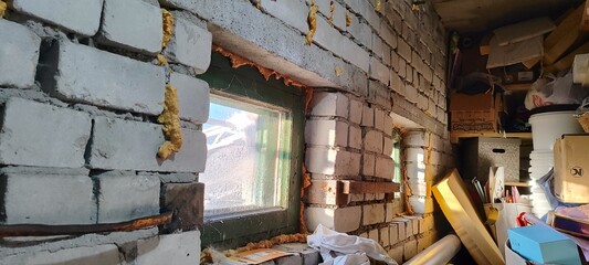 Unfinished brick wall with windows sealed with expanding foam. Interior of a basement during renovation. DIY home improvement and construction concept