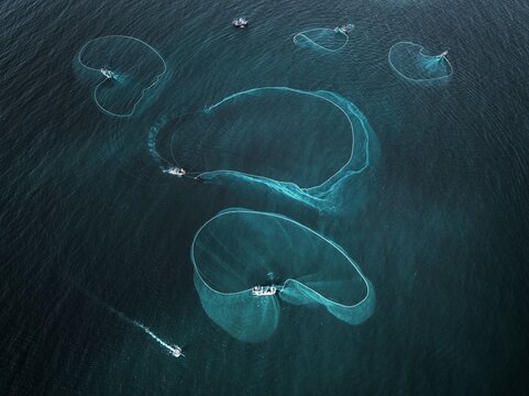 Aerial view of fishing boats casting nets into the deep blue sea, creating mesmerizing patterns on the water's surface, Tuy Hoa, Phu Yen, Vietnam.