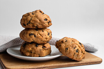 Photo stack fragrant cookies with raisins and nuts on white plate. Homemade baked goods against light background.