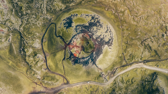Aerial view of a volcanic crater with a vibrant red center surrounded by dark lava flows and green mossy terrain, Akureyri, Rangarbing ytra, Iceland.