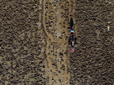 Aerial view of a tractor cutting a deep furrow through the dark, rich soil of a vast agricultural field, Klaten Regency, Central Java, Indonesia.