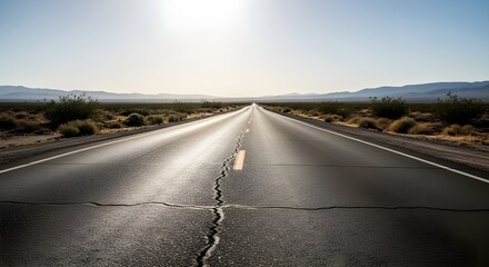 Straight road with a crack runs into the distance under a bright sun framed by shrubs and distant mountains