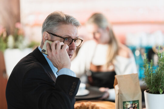Middle aged businessman seated at a bar talks on his smartphone showing a confident professional moment in a relaxed environment