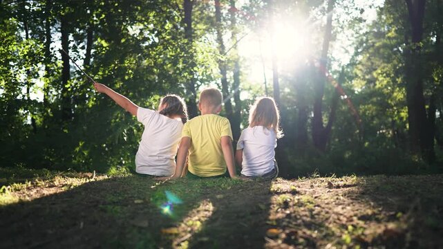 Kid sits with friend on grass kid and friend sit side by side near tree line backlight sunlight filters through forest canopy summer nature mood quiet play soft shadow pattern on ground warm bond link
