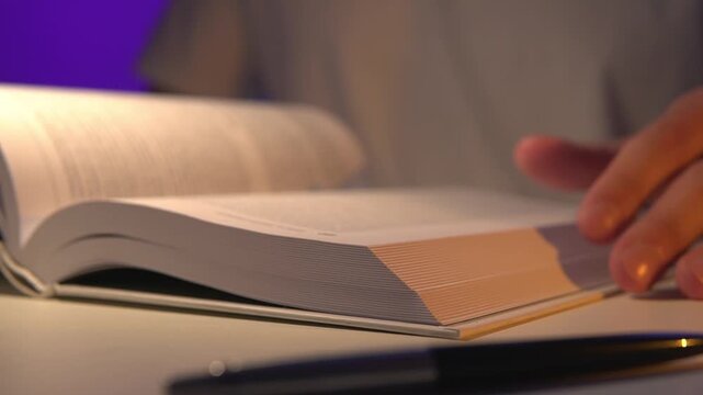 cinematic close-up of a student or professional hand quickly flipping book pages during intense reading or research session at night