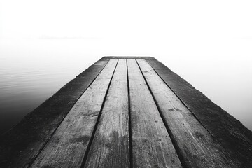 A wooden pier extends into a tranquil, foggy lake under a bright, misty sky. The monochrome scene evokes solitude and minimalist beauty.