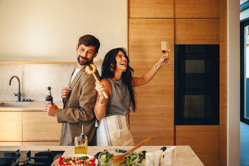 Playful couple enjoying good times cooking and drinking together in modern kitchen