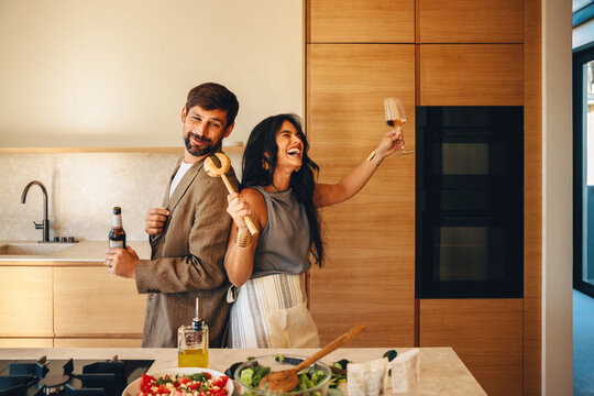 Playful couple enjoying good times cooking and drinking together in modern kitchen