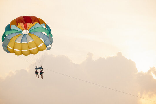 Two people parasailing at sunset with colorful parachute against a serene sky