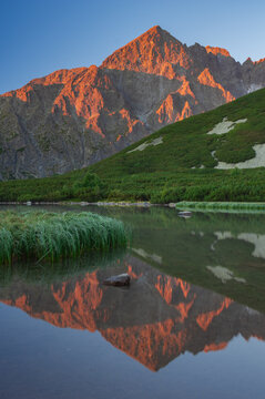 View of a mountain's rugged peak ablaze with the warm hues of the setting sun, mirrored perfectly in the tranquil lake below, Biele pleso tarn, Presovsky kraj, Slovakia.